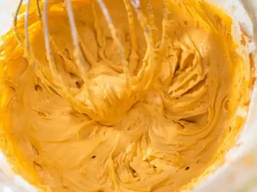 Mieszanie puszystego, złocistego kremu do tortu z mascarpone za pomocą trzepaczki miksera.