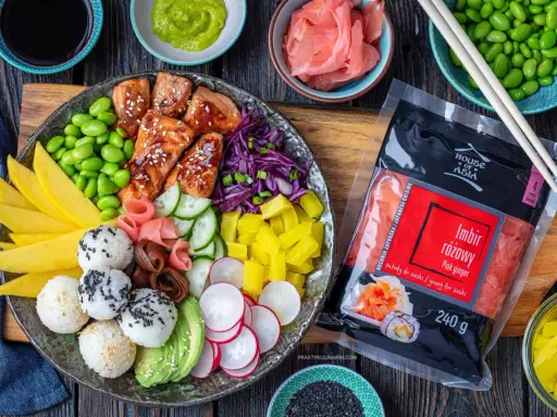 Kolorowy bowl z lososiem, ryżowymi kulkami, mango, awokado, edamame i marynowanym imbirem. Obok opakowanie różowego imbiru.