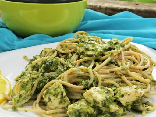 Pyszny makaron z pesto i kurczakiem, podany z plasterkami cytryny.