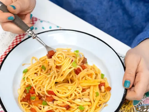 Pyszny obiad bez mięsa: spaghetti z pomidorami, fasolką i szczypiorkiem na talerzu.