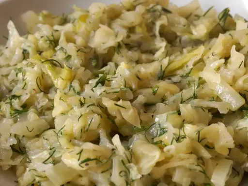 Młoda kapusta zasmażana z koperkiem, podana w białej misce. Danie wygląda na delikatne i aromatyczne.