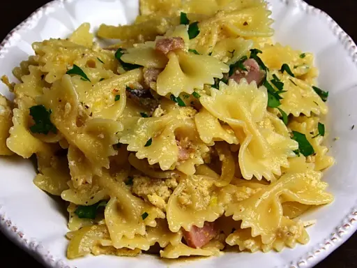 Pyszny makaron farfalle z jajkiem, kawałkami szynki i posiekaną natką pietruszki, podany w białej misce.