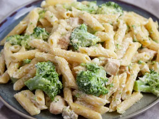 Penne z kurczakiem i kremowym sosem, w którym dominują zielone różyczki brokułów. Danie posypane startym parmezanem.
