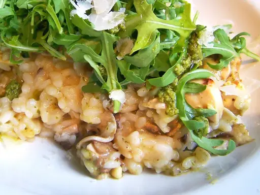 Kremowe risotto z pieczarkami, polane zielonym pesto i posypane parmezanem, udekorowane świeżą rukolą.