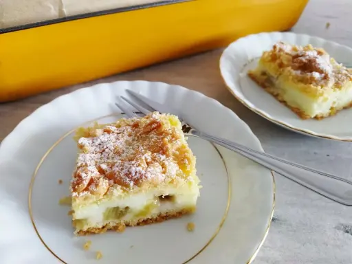 Pyszne ciasto z rabarbarem i budyniem, posypane cukrem pudrem, czeka na talerzyku. Idealne na deser!