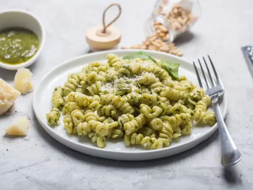 Pyszny makaron z pesto, posypany parmezanem, z dodatkiem świeżej bazylii i orzeszków piniowych.