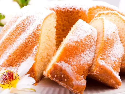 Szybka babka wilgotna, oprószona cukrem pudrem, z widocznymi kawałkami ciasta i ozdobiona kwiatem.