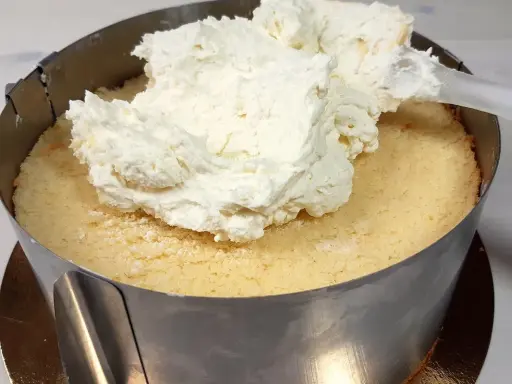 Nakładanie puszystego kremu z mascarpone na biszkopt w tortownicy.