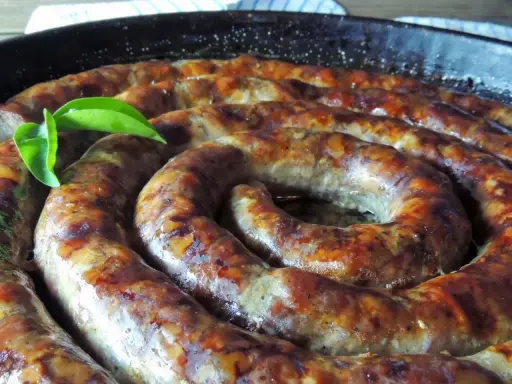 Złocista, pieczona biała kiełbasa w kształcie spirali, skropiona tłuszczem, z zielonym listkiem.