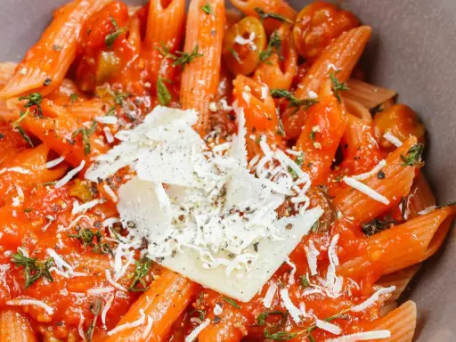 Penne w sosie pomidorowym z oliwkami i parmezanem. Idealny szybki obiad z makaronem, doprawiony ziołami.