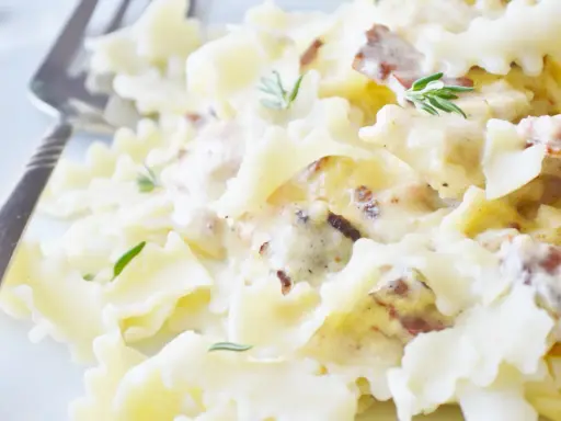 Pyszny makaron farfalle w kremowym sosie śmietanowym z kawałkami boczku i świeżym rozmarynem.