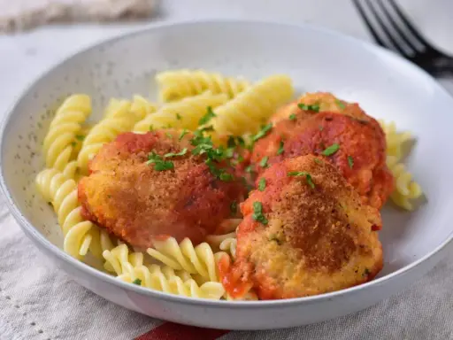Elegancki obiad dla gości: pulpeciki w sosie pomidorowym z makaronem fusilli, posypane natką pietruszki.