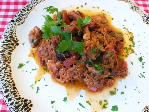 Pyszny bigos z kiszonej kapusty z kawałkami mięsa i kiełbasy, udekorowany natką pietruszki.