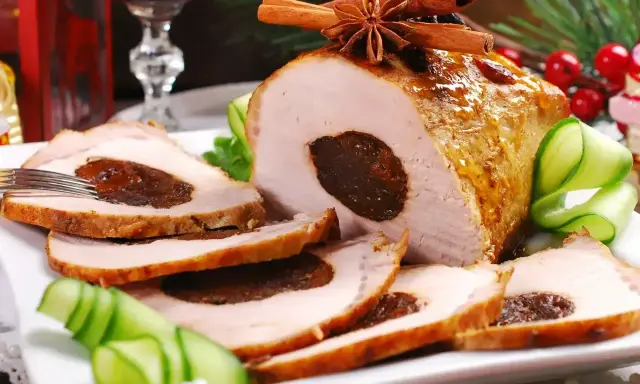 Pyszny schab ze śliwką, pieczony z przyprawami, podany z ogórkiem i dekoracjami świątecznymi.