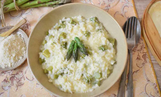 Kremowe risotto ze szparagami, posypane parmezanem, z kilkoma zielonymi szparagami na wierzchu.