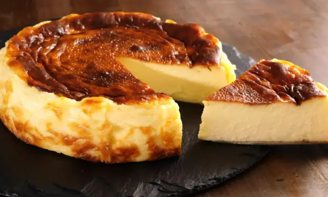 Pyszny, lekko przypieczony sernik Ani gotuje się na ciemnej desce. Jeden kawałek już czeka na spróbowanie.