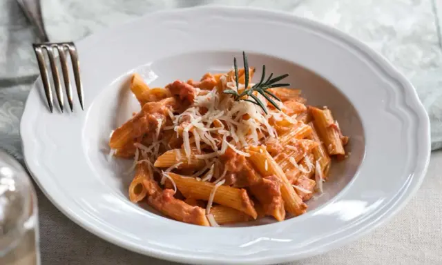 Penne alla vodka z kremowym sosem pomidorowym, posypane parmezanem i udekorowane gałązką rozmarynu.