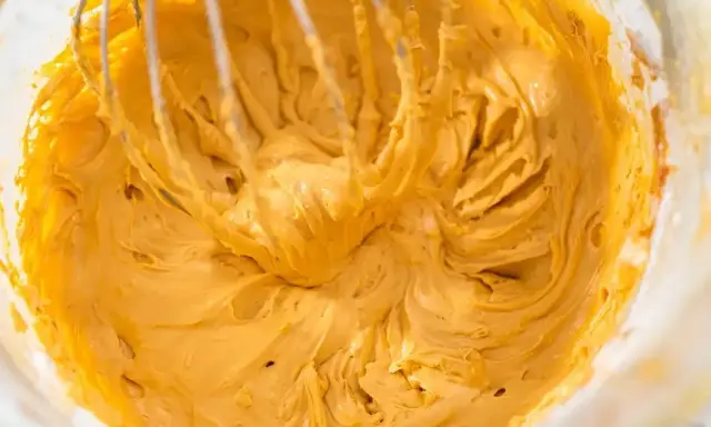 Mieszanie puszystego, złocistego kremu do tortu z mascarpone za pomocą trzepaczki miksera.