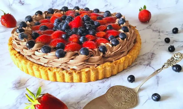 Pyszna tarta z owocami: kruchy spód, czekoladowy krem i świeże truskawki z borówkami. Idealna na deser!