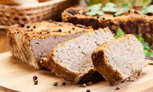 Domowy pasztet drobiowy z mięsa z rosołu, pokrojony na desce, ozdobiony ziarnami pieprzu.