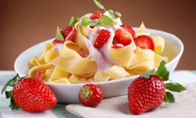 Pappardelle z kremowym sosem i świeżymi truskawkami, ozdobione listkami mięty. Letnia uczta z makaronem i truskawkami.