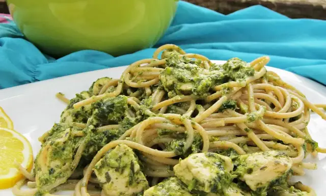 Pyszny makaron z pesto i kurczakiem, podany z plasterkami cytryny.