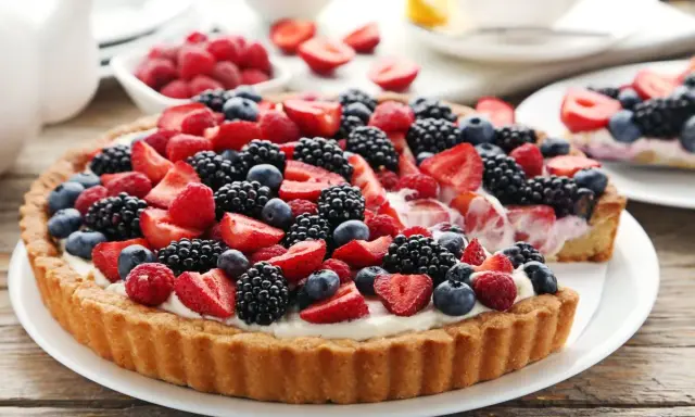Pyszna tarta z mascarpone, udekorowana malinami, jeżynami i borówkami.