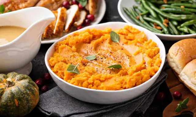 Aksamitne puree z batata, ozdobione listkami ziół, stanowi centralny punkt świątecznego stołu. Obok pieczony indyk, fasolka szparagowa i bułeczki.