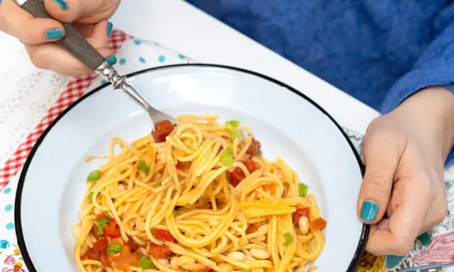 Pyszny obiad bez mięsa: spaghetti z pomidorami, fasolką i szczypiorkiem na talerzu.
