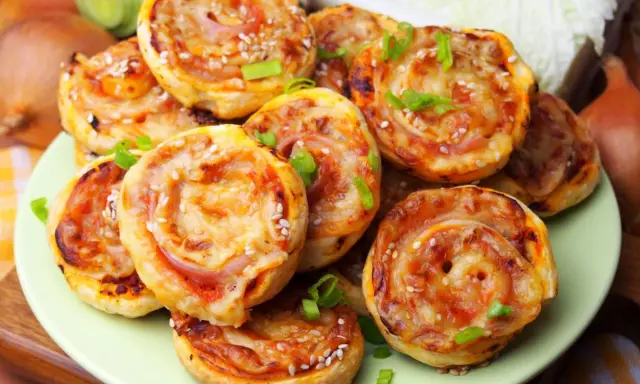 Pyszne pizzerinki z ciasta francuskiego, posypane sezamem i szczypiorkiem, ułożone na talerzu.