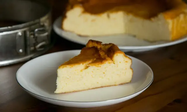 Puszysty sernik z mlekiem skondensowanym, z lekko zarumienioną skórką, na talerzyku. Obok forma do pieczenia.