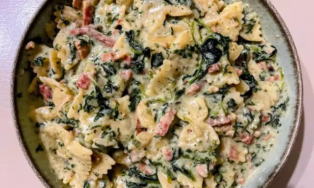 Pyszny makaron farfalle w kremowym sosie ze szpinakiem i kawałkami boczku.