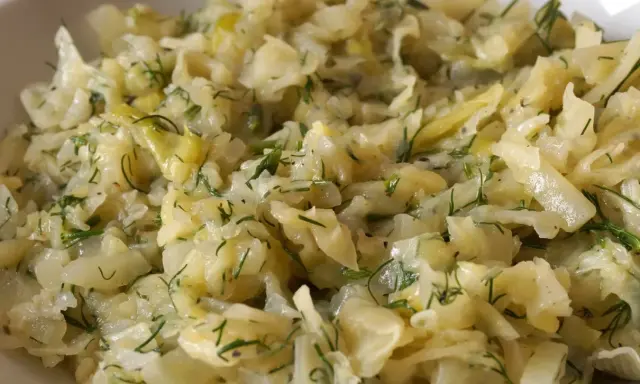 Młoda kapusta zasmażana z koperkiem, podana w białej misce. Danie wygląda na delikatne i aromatyczne.