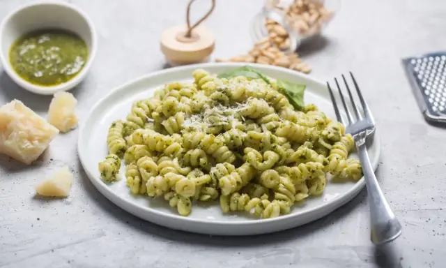 Pyszny makaron z pesto, posypany parmezanem, z dodatkiem świeżej bazylii i orzeszków piniowych.