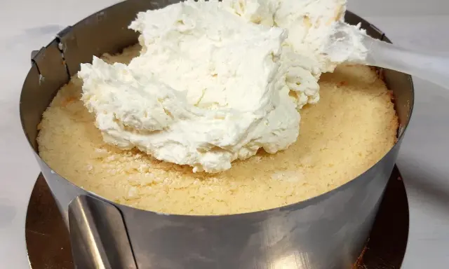 Nakładanie puszystego kremu z mascarpone na biszkopt w tortownicy.
