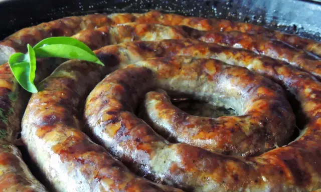 Złocista, pieczona biała kiełbasa w kształcie spirali, skropiona tłuszczem, z zielonym listkiem.