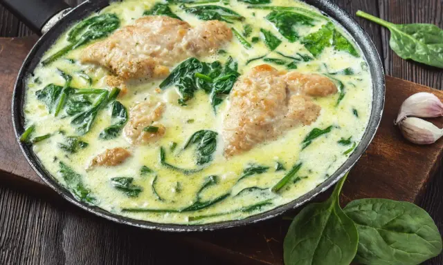 Pyszny kurczak ze szpinakiem w kremowym sosie, podany na patelni. Aromatyczne danie, które zachwyci każdego.