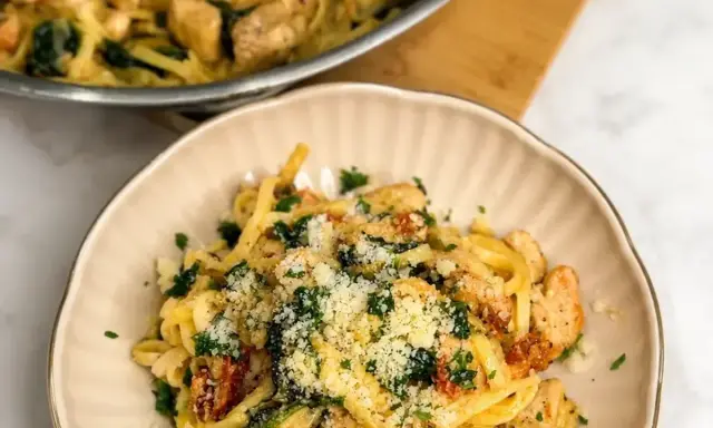 Pyszny makaron z kurczakiem i suszonymi pomidorami, posypany parmezanem i natką pietruszki.