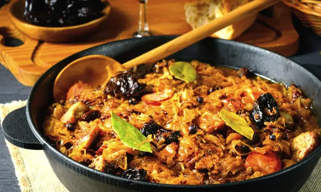 Ania gotuje pyszny bigos w żeliwnym naczyniu, pełen kapusty, mięsa i śliwek.