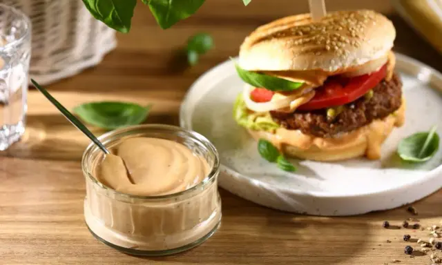 Pyszny sos do hamburgerów w słoiczku, obok soczystego burgera z dodatkami. Idealny do każdej kanapki.
