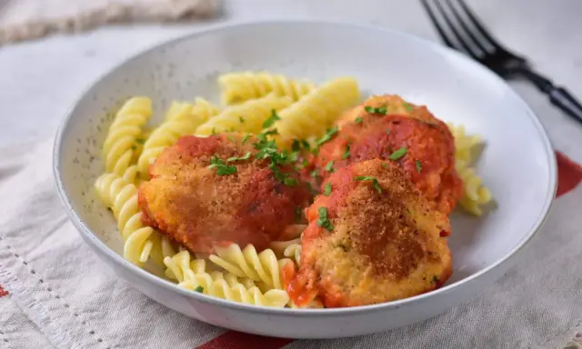Elegancki obiad dla gości: pulpeciki w sosie pomidorowym z makaronem fusilli, posypane natką pietruszki.
