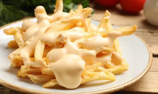 Chrupiące frytki z airfryer polane kremowym sosem serowym. Idealna przekąska, która rozpływa się w ustach.