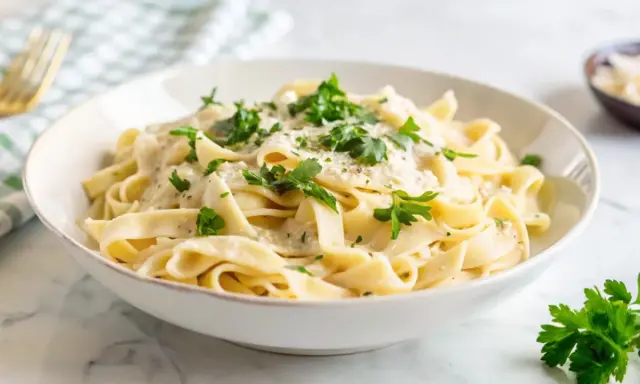 Pyszny makaron z pieczarkami w kremowym sosie, posypany świeżą natką pietruszki i parmezanem. Idealny na szybki obiad.