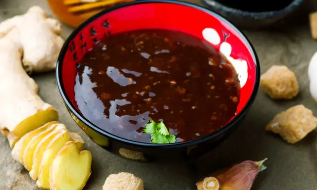 Miseczka z sosem teriyaki, obok świeży imbir, czosnek i cukier. Idealne składniki do przygotowania domowego sosu teriyaki.