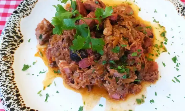 Pyszny bigos z kiszonej kapusty z kawałkami mięsa i kiełbasy, udekorowany natką pietruszki.