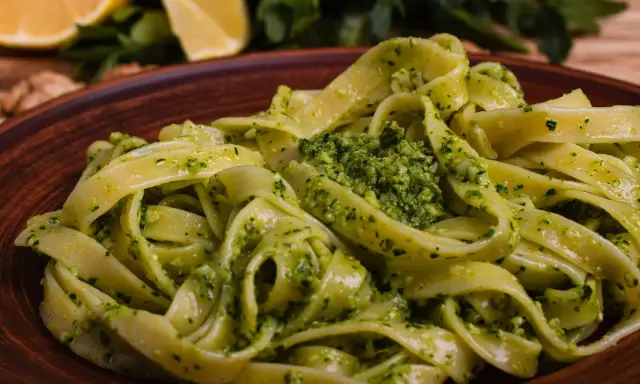 Tagliatelle z aromatycznym pesto z rukoli, podane na brązowym talerzu, z cytryną i orzechami w tle.