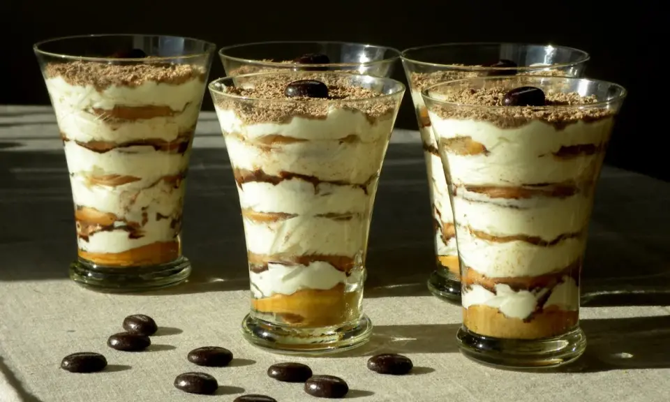 Pyszne tiramisu w pucharkach, warstwowo ułożone z kremem i biszkoptami, posypane czekoladą i kawą.