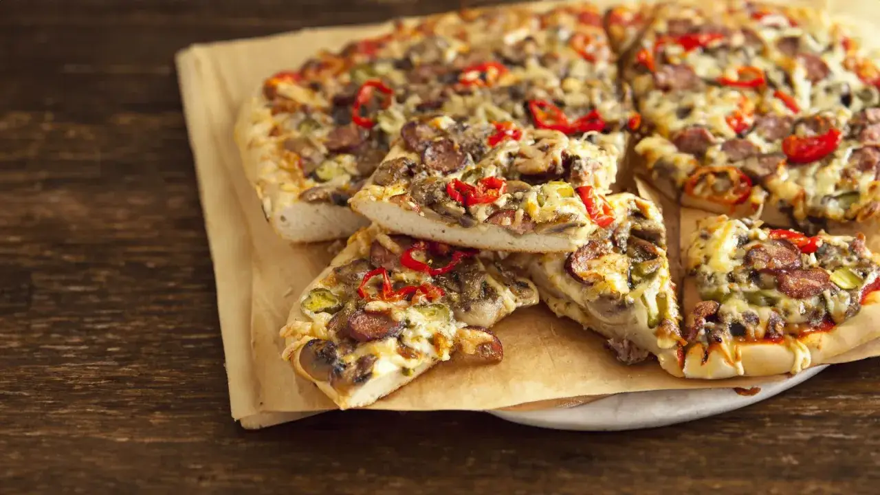 Pyszna pizza na grubym cieście z kiełbasą, pieczarkami i papryczką chili, pokrojona na kawałki.