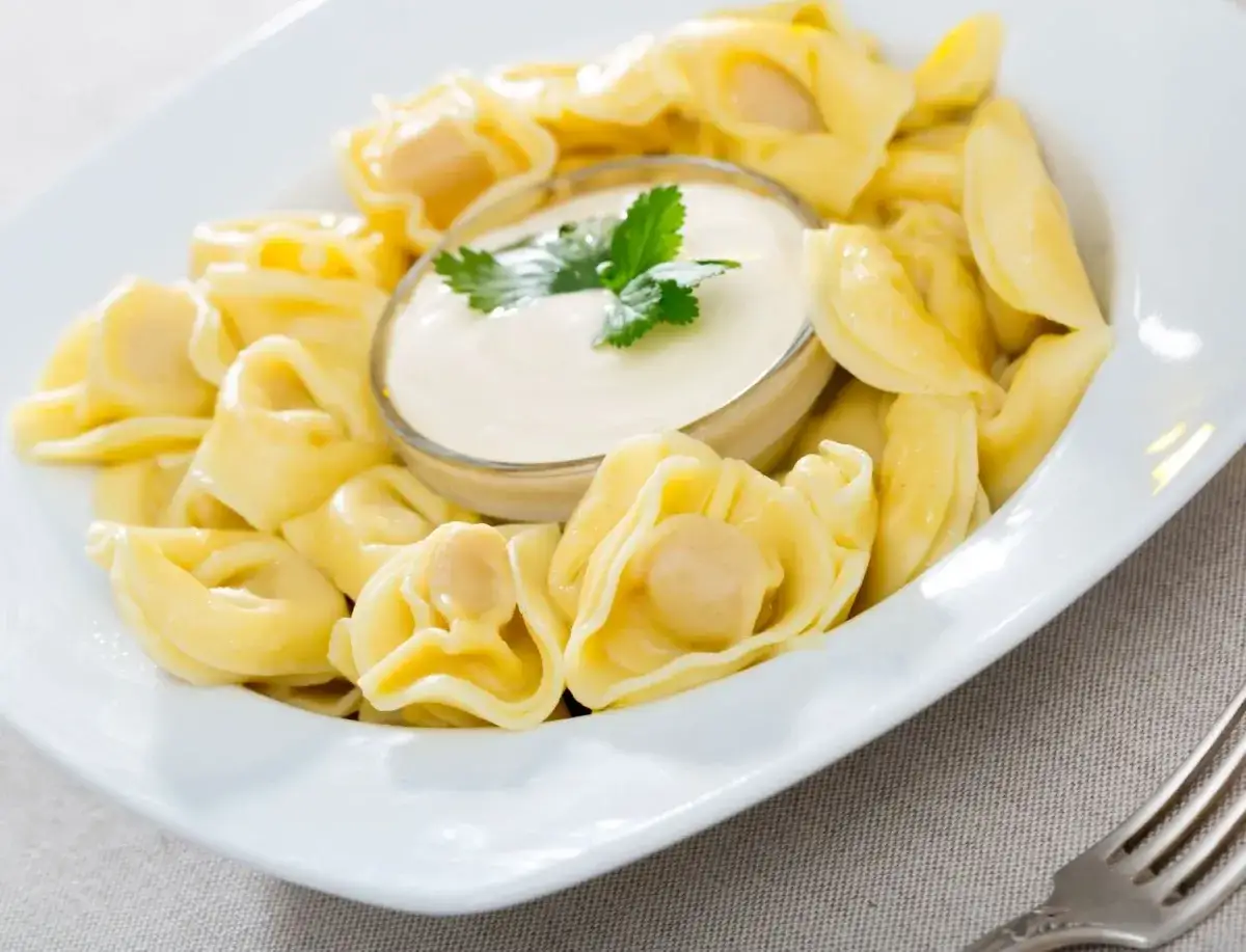 Pyszne tortellini podane z kremowym sosem śmietanowym do makaronu, udekorowane natką pietruszki.