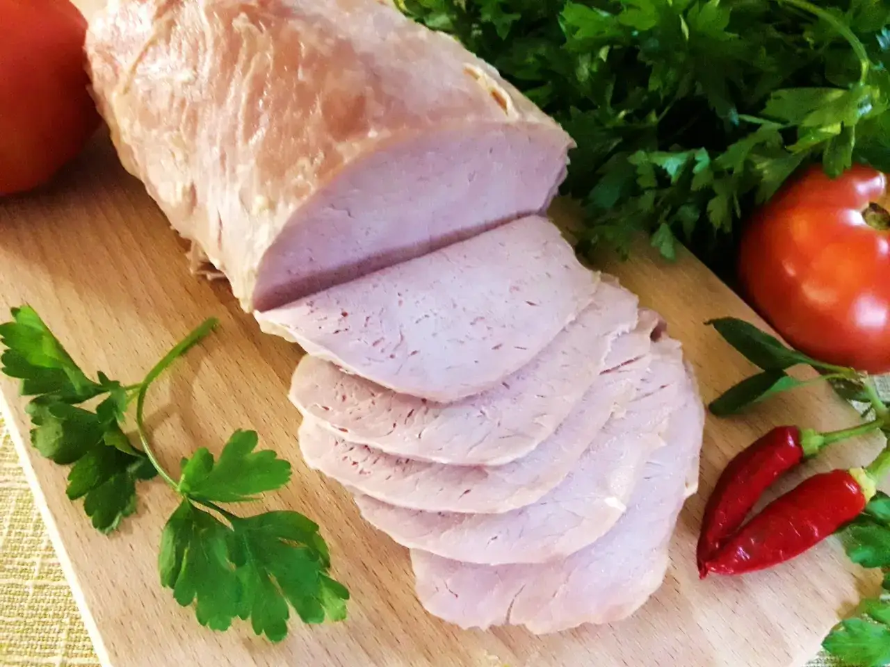 Pokrojony schab gotowany 2 razy po 5 minut, podany z pomidorami, papryczkami chili i natką pietruszki na desce.